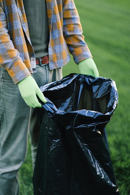 A person wearing a white glove with a blue watch on their wrist is holding a large white woven polypropylene sack filled with assorted garden waste, including small branches, twigs, dead leaves, and i
